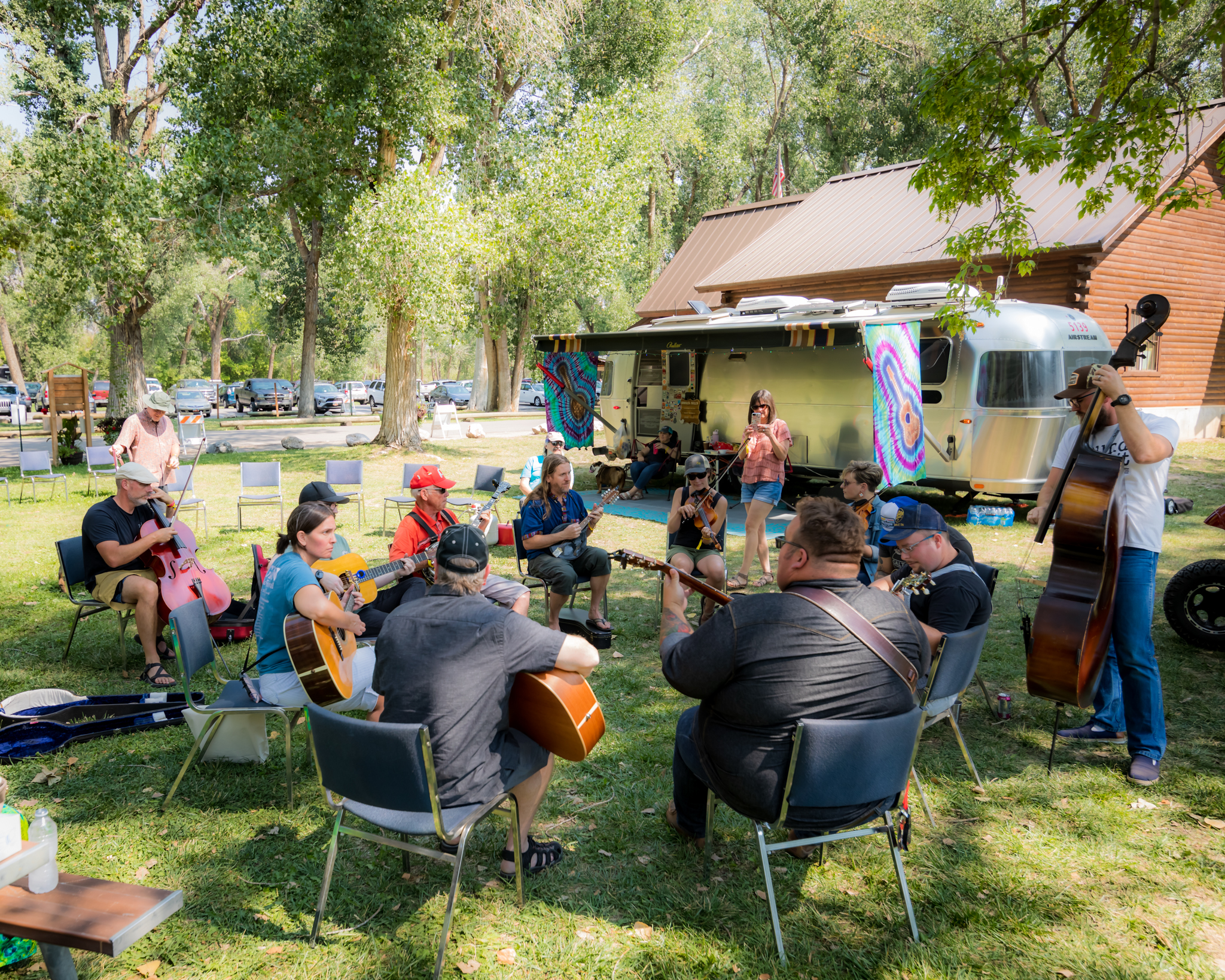 People sitting in a circle with guitars and other instruments playing together in front of an airstream trailer