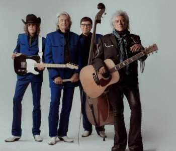 Marty Stuart and His Fabulous Superlatives, Marty holds and acoustic guitar, 3 other band members behind him hold an upright bass, drumsticks, and an electric guitar.